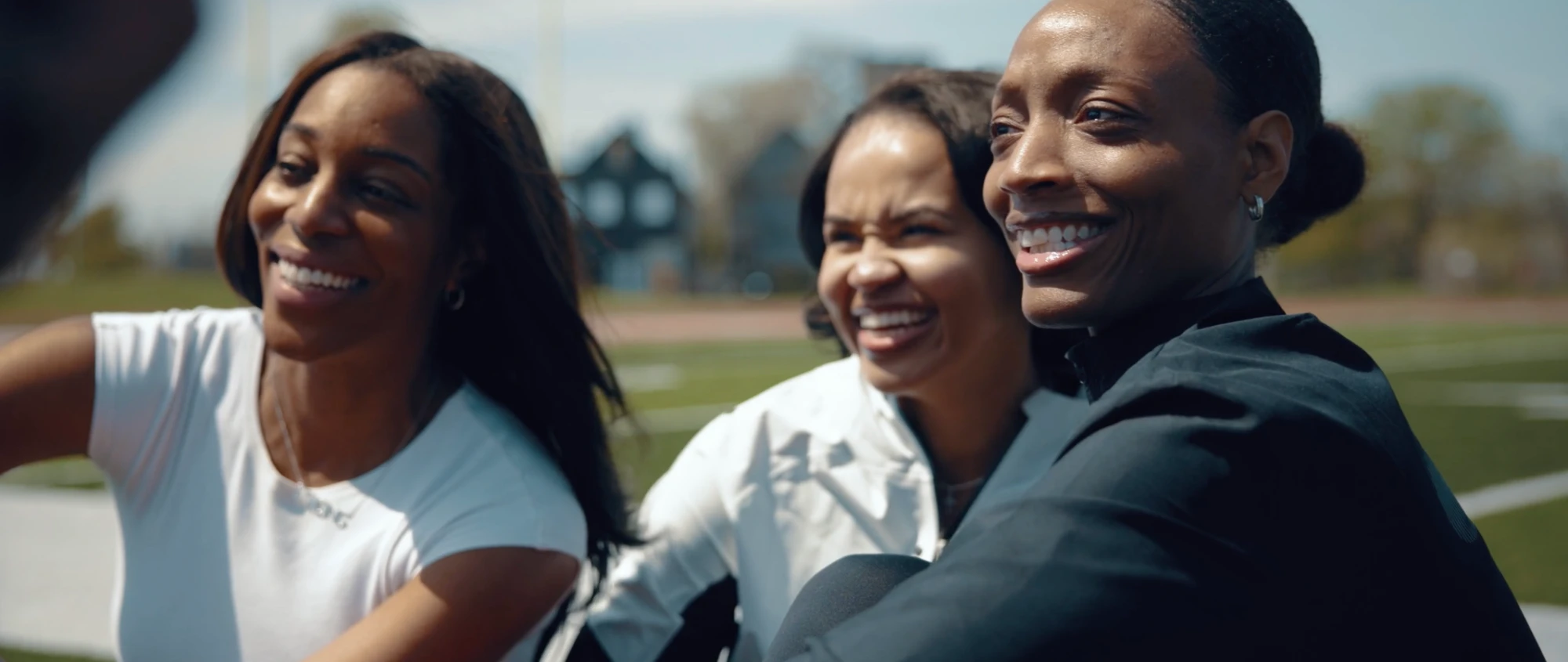 Three runners smiling together on a sunny track field
