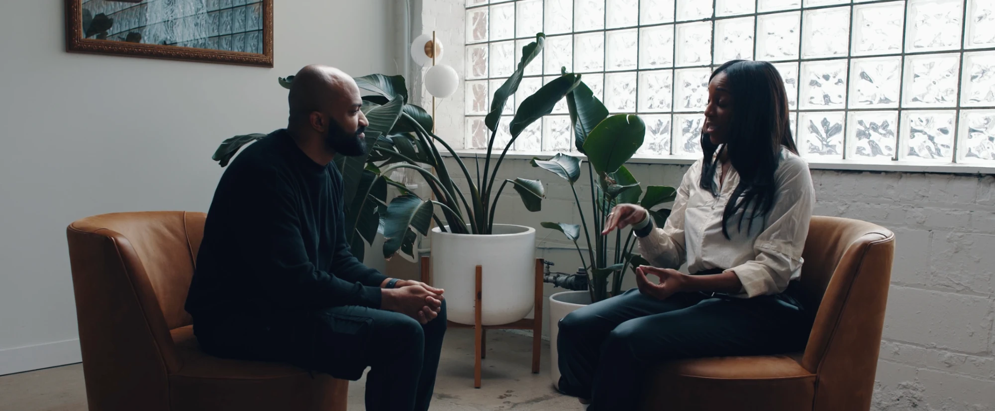 A second interview in the same studio beside a glass-block window